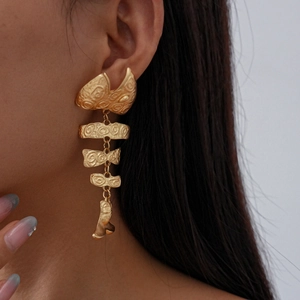 Detailed view of long golden metal earrings with fishbone design and spiral textures