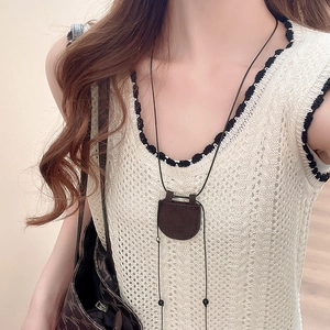 Détail d'un pendentif mini sac en cuir marron avec cordon noir sur un gilet en maille