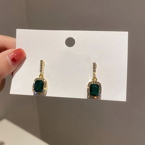 Detailed view of rectangular emerald gemstone earrings with diamond halo on display card