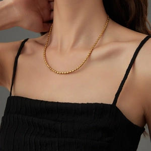 Close-up of a gold-plated bamboo link bead necklace worn by a model on the collarbone