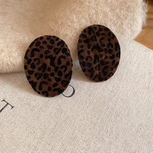 Macro view of oval leopard print earrings with flocked texture on beige fabric