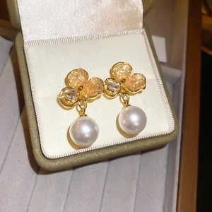 Vue macro de boucles d'oreilles trèfle avec pétales dorés et pendentif perle blanche