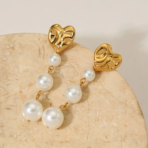 Elegant gold heart earrings with white pearl tassels on beige marble surface