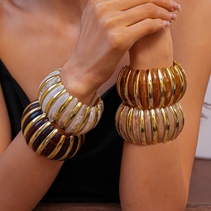 Detail of stacked acrylic resin bangles with gold metal accents in amber and pink tones