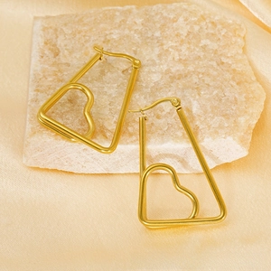 Détail de boucles d'oreilles cœur géométriques en acier doré 18K sur satin de luxe