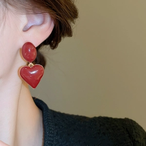 Detail view of a model wearing a burgundy heart enamel earring with gold base