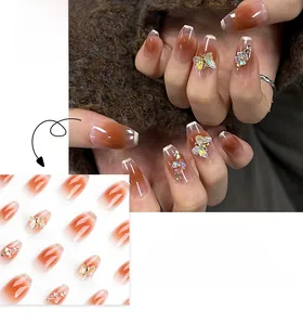 Detail of press-on nails with butterfly charms, rhinestones and orange gradient finish
