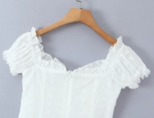 Detail of white lace top featuring square neck, puff sleeves and floral hollow patterns
