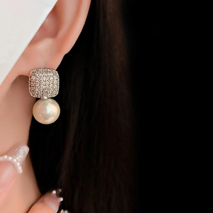 Close-up of square zircon stud earring with large pearl drop on a model