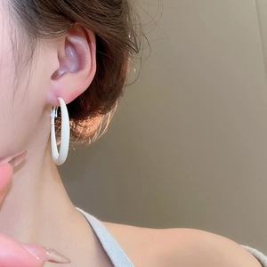 Close-up of minimalist white circular hoop earrings worn by a model in soft lighting
