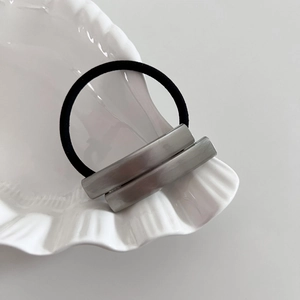Close-up of minimalist hair tie with silver brushed metal accents on white shell plate