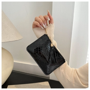 Detail of black crocodile texture handbag with golden chain handle and tassel accents