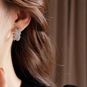 Detailed macro view of silver C-shaped earrings with micro-inlaid zircon and lava texture