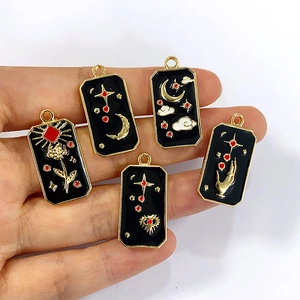 Hand holding mystical tarot-style alloy charms with black enamel and gold moon star patterns