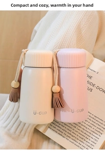 Mini insulated cups in off-white and pink with tassels held by hands in a cozy setting