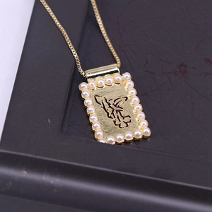 Detail of square gold pendant with pearl trim and hollow figure on a dark tray