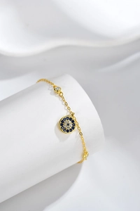 Macro detail of gold evil eye bracelet with blue and white crystals on white stand