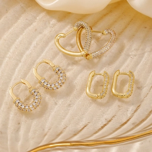 Dettaglio di tre orecchini placcati in oro con zirconi a forma di cuore e design a U