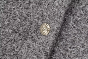 Close-up of golden vintage textured button on premium grey boucle tweed jacket fabric