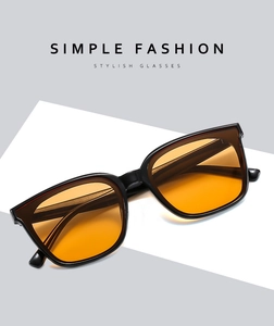Detail of square black frame sunglasses with transparent orange lenses on white stand