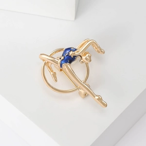 Detail of a golden gymnastic girl brooch with dark blue enamel finish on white background