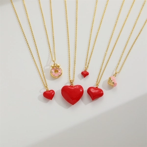 Golden necklace set with red enamel heart pendants and pink doughnut charm on grey background