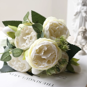Close-up of white artificial silk peonies with lush green leaves in a minimalist setting