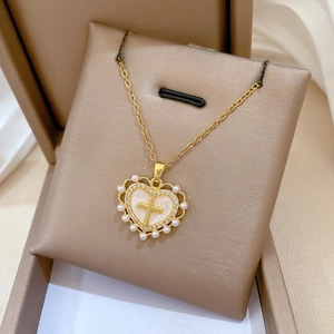 Detailansicht goldener Herzanhänger mit Kreuz und Perlen auf einem Samtständer