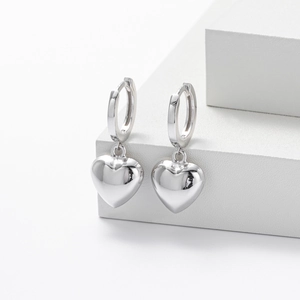 Close-up of polished silver 3D heart-shaped earrings on a white geometric stand