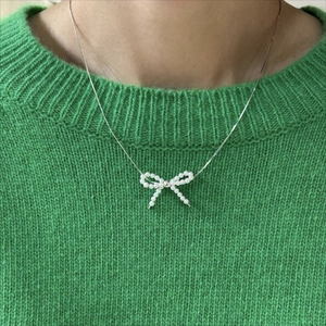 Detail of 925 sterling silver bow necklace with white pearls on a green sweater