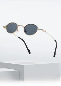 Detail of oval metal sunglasses with gold frame and dark lenses on a white pedestal