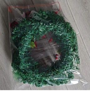 Detail of a green pine needle Christmas wreath with red berries and bells in clear packaging