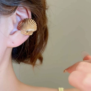 Close-up of golden shell-shaped ear cuff with textured pattern on ear without piercing