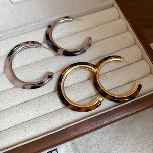 Detailed close-up of C-shaped acetate hoop earrings in silver and gold metal finishes