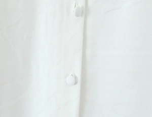 Detail of white linen fabric with minimalist fabric-covered round buttons on the collar