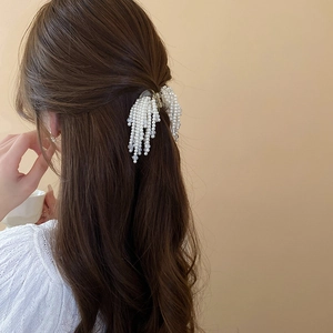 Detail view of artificial pearl tassel hair claw clip worn in an elegant half-up style