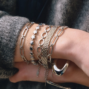 Detail of silver stainless steel paperclip and star charm bracelets layered on wrist