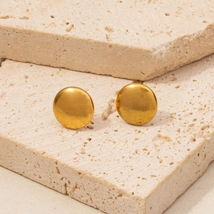 Close-up of golden matte round stud earrings on a textured stone surface