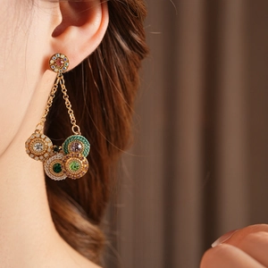 Détail de boucles d'oreilles vintage dorées avec strass colorés et pompons tressés
