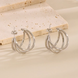 Close-up of silver multilayer C-shaped geometric earrings on a textured stone surface