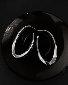 Polished silver oval hoop earrings displayed on a dark circular plate for high-end contrast