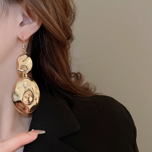 Close-up of elegant gold irregular textured earring worn by model in black suit
