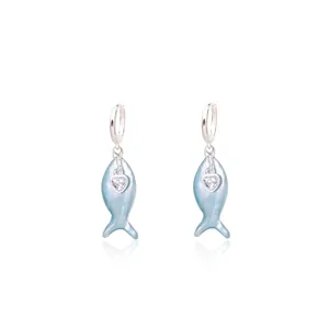 Detail view of silver fish-shaped earrings with blue pearlescent body and heart zircon