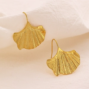 Gros plan détaillé de boucles d'oreilles feuille de ginkgo dorée sur un tissu blanc texturé
