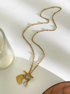 Detailed view of gold heart pendant with Mom engraving and OT toggle clasp on white surface