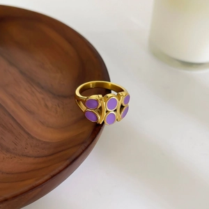 Luxury gold stainless steel ring with purple enamel drops on a dark wooden stand