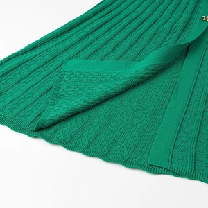 Détail d'une robe en tricot vert avec motifs torsadés et fente à bouton doré élégante