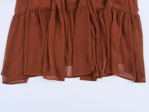 Detail eines rotbraunen Chiffon-Kleides mit Rüschen und gestuftem, gefaltetem Saum