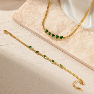 Golden snake chain jewelry set with emerald heart pendants on stone and silk