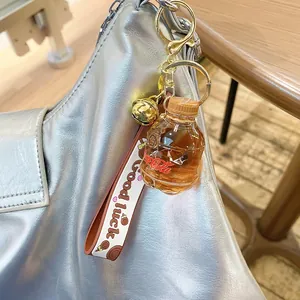 Creative soda bottle keychain with pink strap and golden bell on silver leather bag